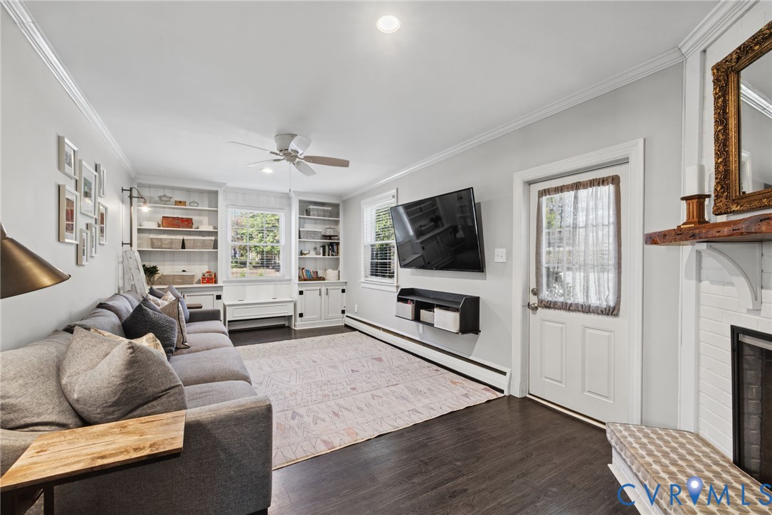 Living area featuring wood-finish flooring, built-in floor-to-ceiling cabinetry, recessed lighting, ceiling fan, and a fireplace with a rustic mantel