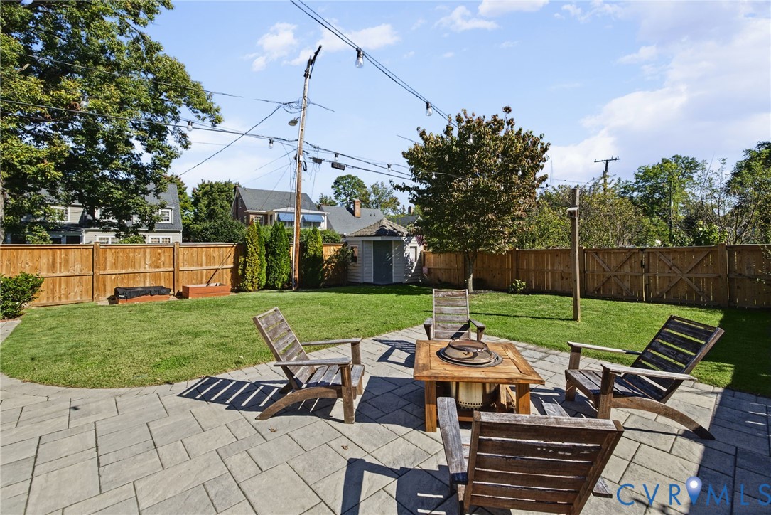 Rear yard featuring a stone paver patio, wood privacy fencing, a storage shed, and manicured lawn space