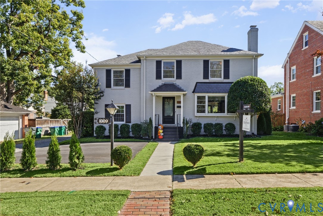 Two-story residence featuring a painted brick exterior, dark window shutters, a prominent chimney, a covered front entryway, and an asphalt driveway Two-story residence featuring a painted brick exterior, dark window shutters, a prominent chimney, a covered front entryway, and an asphalt driveway
