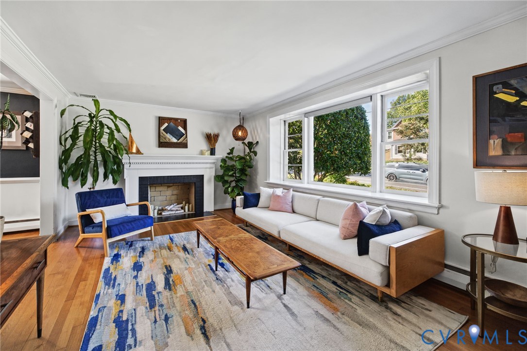 Living area featuring wood-finish flooring, a fireplace with a decorative mantel, and a large picture window Living area featuring wood-finish flooring, a fireplace with a decorative mantel, and a large picture window