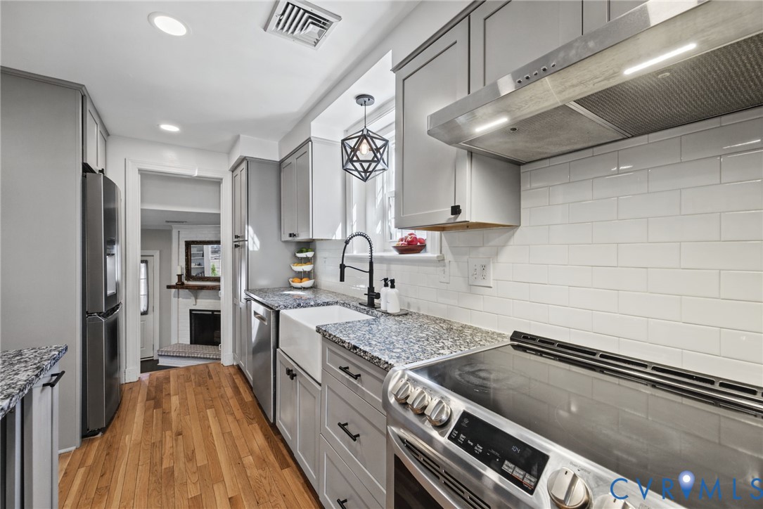 Kitchen featuring gray shaker-style cabinetry, white subway tile backsplash, farmhouse sink with matte black faucet, and stainless steel appliances