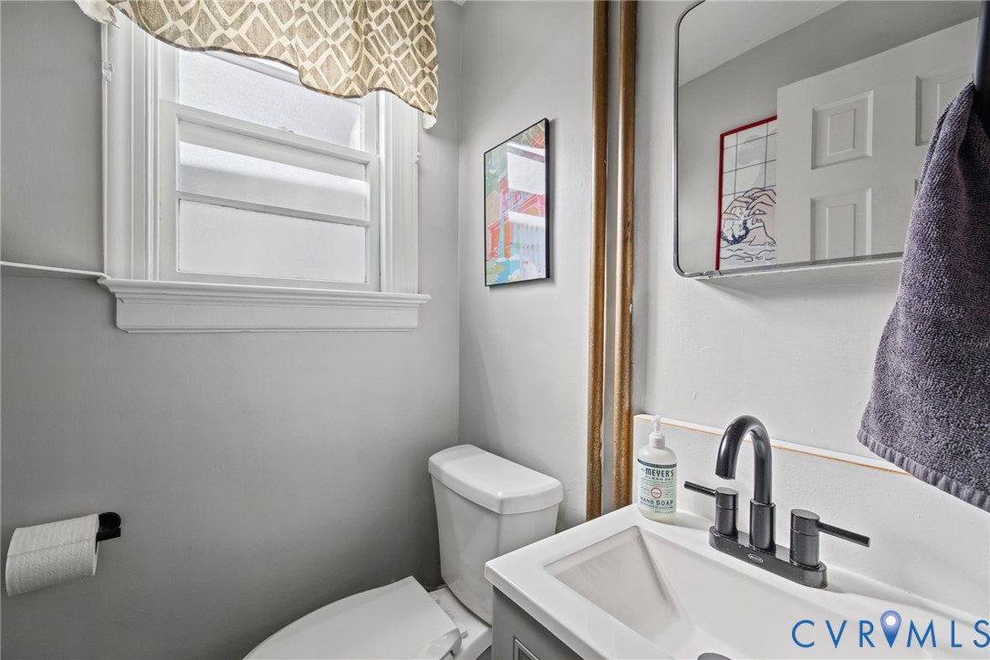 Bathroom featuring a vanity with a white integrated basin, matte black widespread faucet, rectangular wall-mounted mirror, and a double-hung window with decorative trim