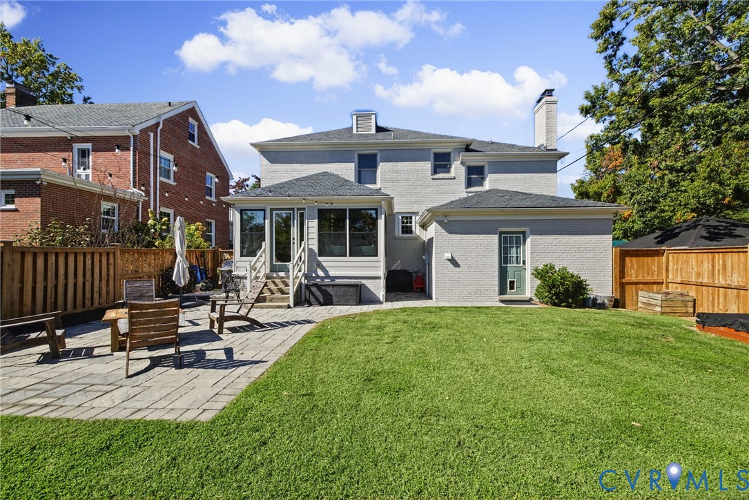 Backyard featuring a paved stone patio, manicured lawn, painted masonry exterior, and wooden privacy fencing