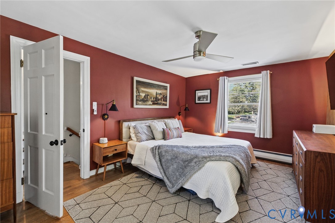 Bedroom featuring wood-finish flooring, a multi-blade ceiling fan, and wall-mounted light fixtures