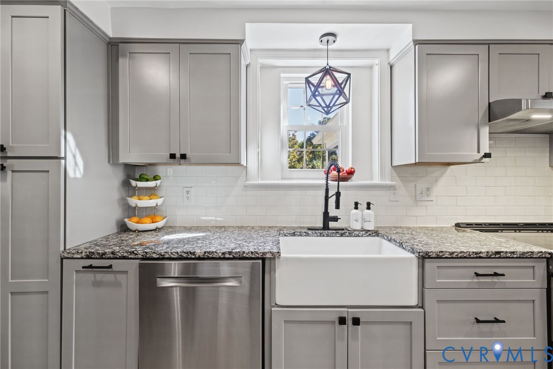 Kitchen featuring grey shaker-style cabinetry, white subway tile backsplash, stone-surface countertops, white apron-front farmhouse sink, and matte black hardware