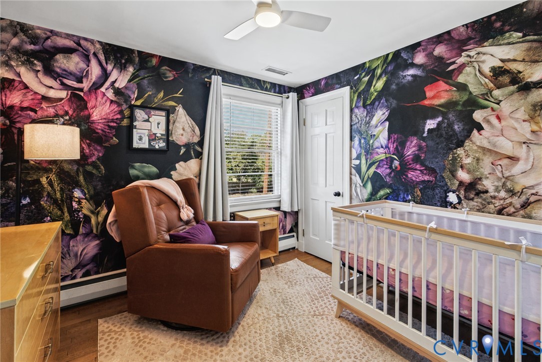 Room featuring floral-patterned wallpaper, wood-finish flooring, a multi-pane window, and a ceiling-mounted light fixture with integrated fan