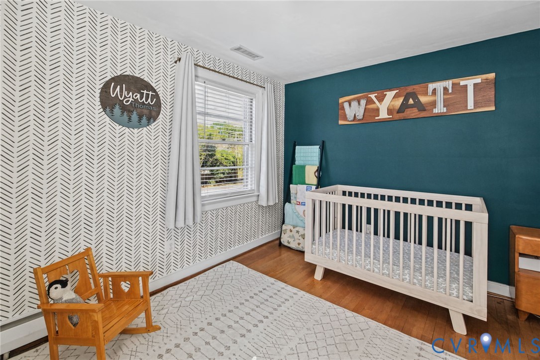 Interior room featuring wood-finish flooring, a patterned accent wall, a solid-colored wall, and a window with horizontal blinds