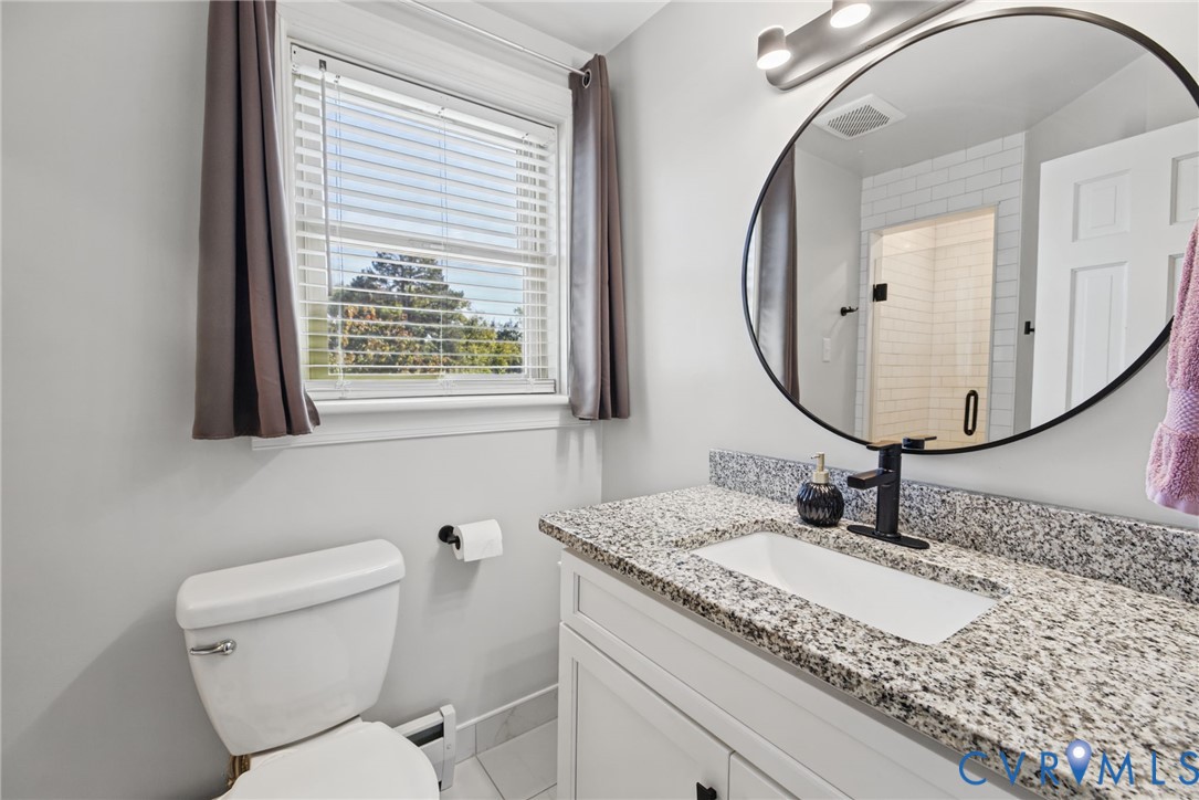 Bathroom vanity featuring a speckled stone countertop, white shaker-style cabinetry, a round mirror, and a matte black single-handle faucet