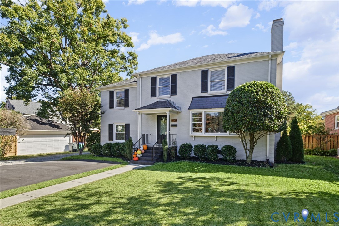 Two-story traditional exterior featuring light-toned brick masonry, black shutters, an asphalt shingle roof, a covered front entryway, and a paved driveway Two-story traditional exterior featuring light-toned brick masonry, black shutters, an asphalt shingle roof, a covered front entryway, and a paved driveway