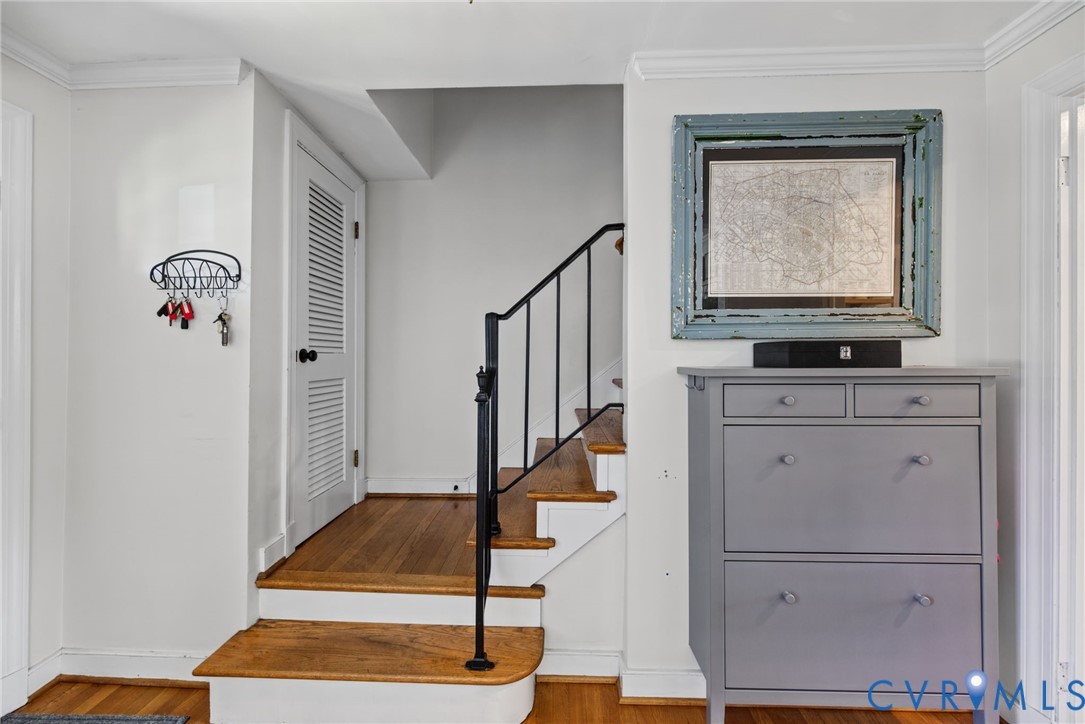 Staircase featuring wood-finish treads, white risers, and a black wrought-iron handrail, accented by crown molding and a louvered closet door Staircase featuring wood-finish treads, white risers, and a black wrought-iron handrail, accented by crown molding and a louvered closet door