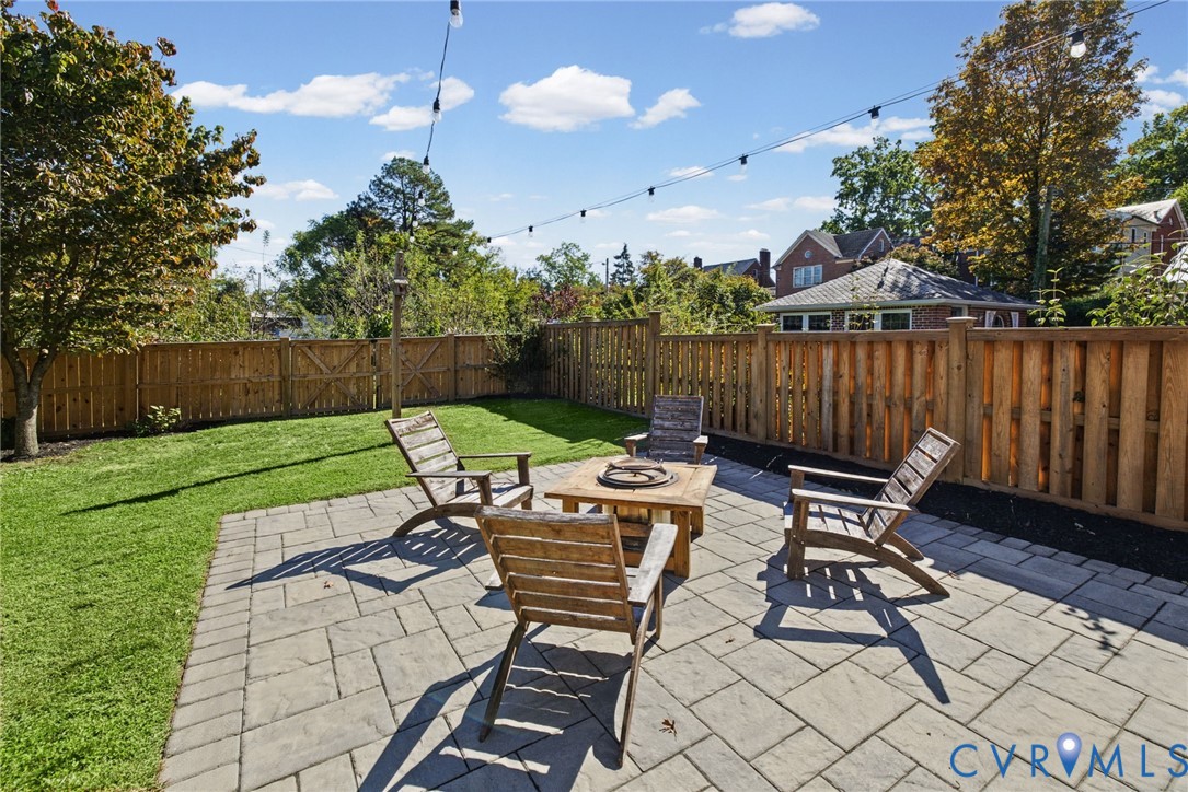 Backyard featuring a paved stone patio, manicured lawn, perimeter wood fencing, and overhead string lighting
