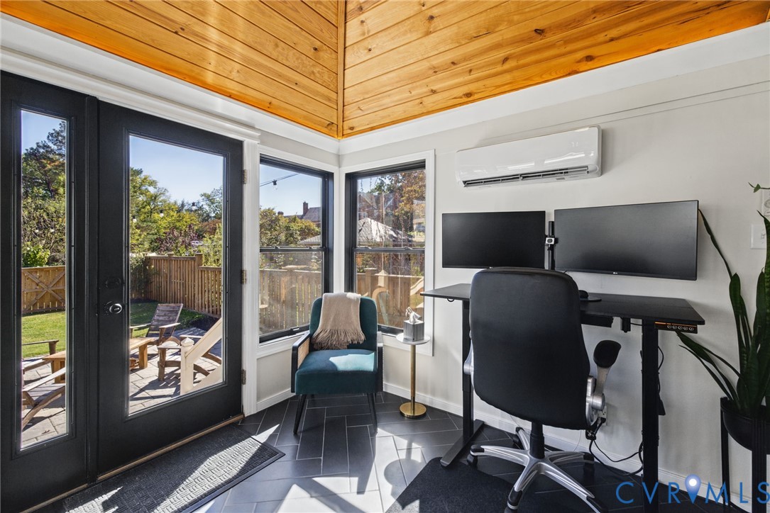 Vaulted wood-plank ceiling, black-framed glass entry door, herringbone-patterned tile flooring, multiple windows, and wall-mounted HVAC unit