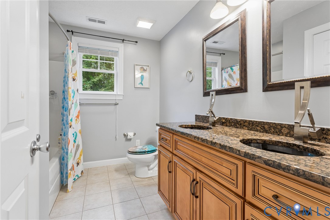 Double vanity featuring a stone-look countertop, integrated dual sinks, wood-finish cabinetry, and framed wall mirrors