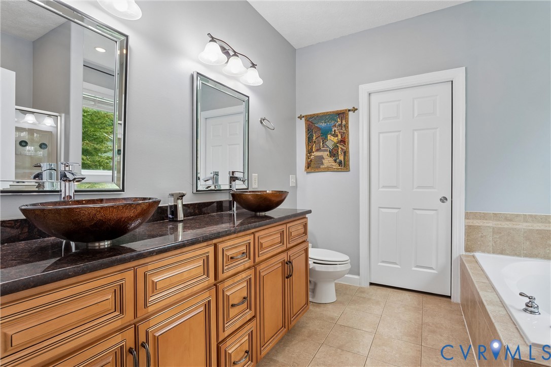 Double vanity featuring medium-tone wood cabinetry, dark stone countertops, bronze-tone vessel sinks, and twin framed mirrors
