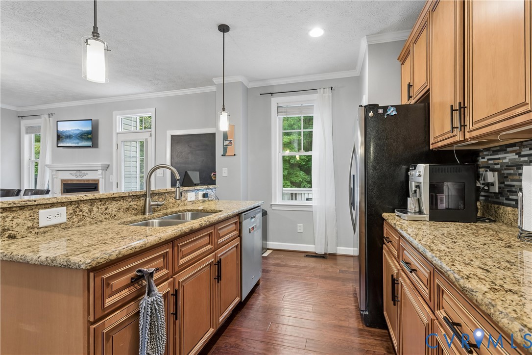 Kitchen featuring stained wood cabinetry, stone countertops, wood-finish flooring, stainless steel under-mount sink with high-arc faucet, and pendant lighting