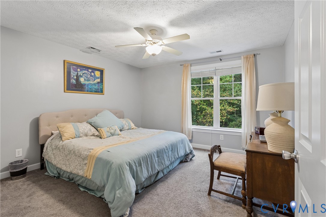 Neutral interior featuring wall-to-wall carpeting, a multi-pane window with natural light, and a ceiling-mounted fan with integrated light fixture