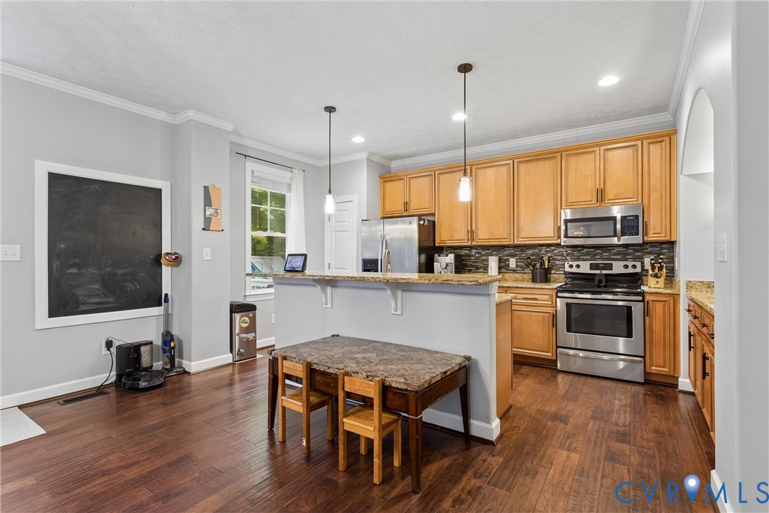 Kitchen featuring wood cabinetry, stainless steel appliances, stone-finish countertops, tile backsplash, and wood-finish flooring
