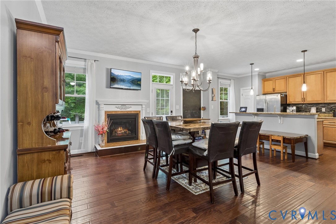 Wood-finish flooring, fireplace with a decorative mantel, kitchen cabinetry with a peninsula, and hanging chandelier lighting