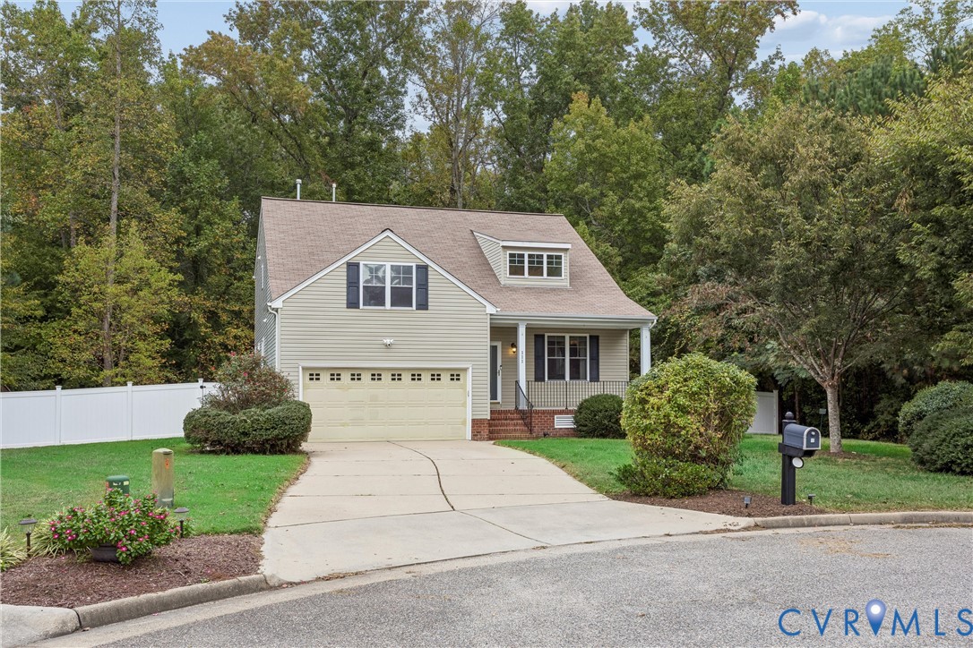 Two-story residence featuring light-toned horizontal siding, a gabled roofline, a two-car garage, and a concrete driveway, complemented by a perimeter privacy fence and manicured landscape Two-story residence featuring light-toned horizontal siding, a gabled roofline, a two-car garage, and a concrete driveway, complemented by a perimeter privacy fence and manicured landscape