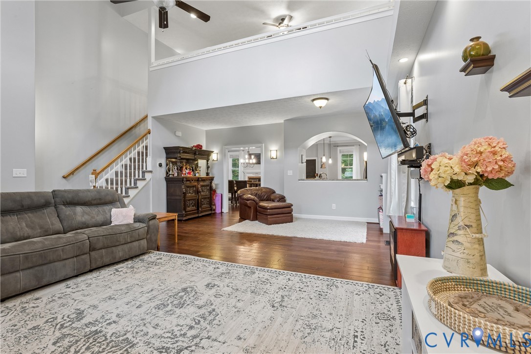 Vaulted ceilings, wood-finish flooring, an arched wall pass-through, and a staircase featuring a wooden handrail
