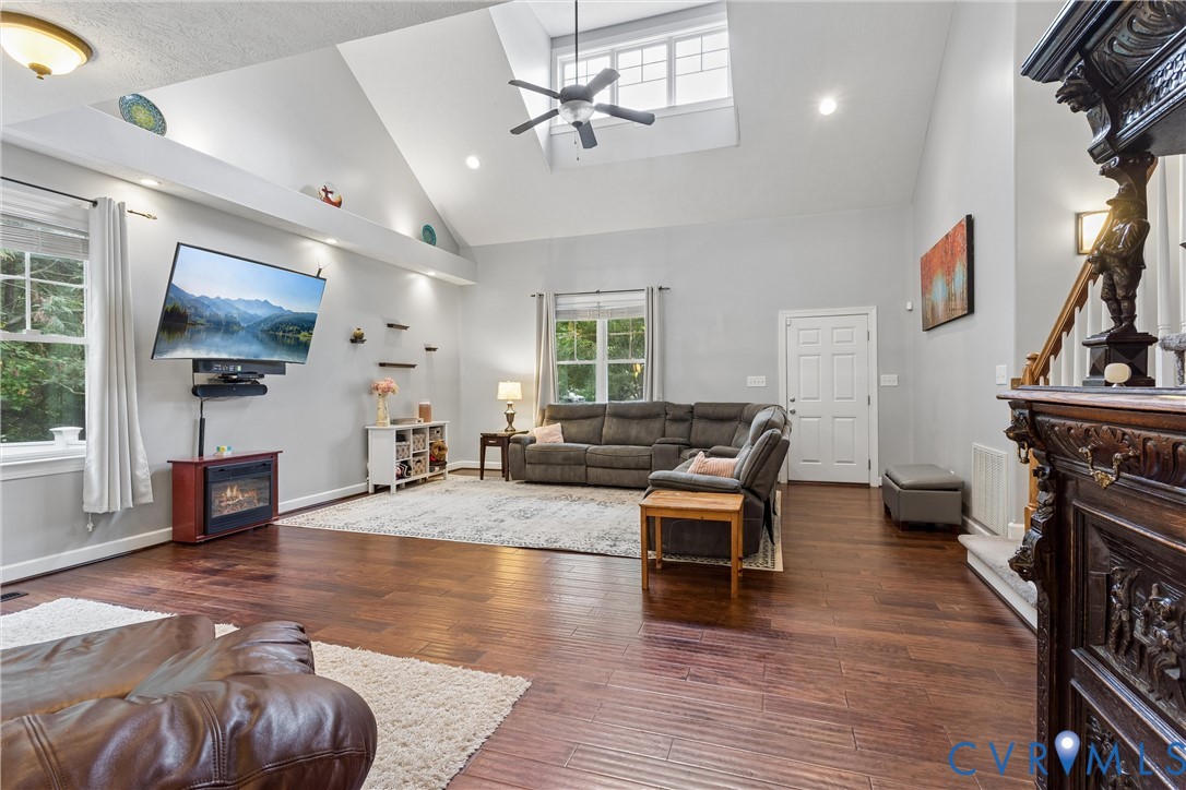 Vaulted ceilings featuring recessed lighting, a transom window, and a central ceiling fan, complemented by wood-finish flooring and an architectural ledge