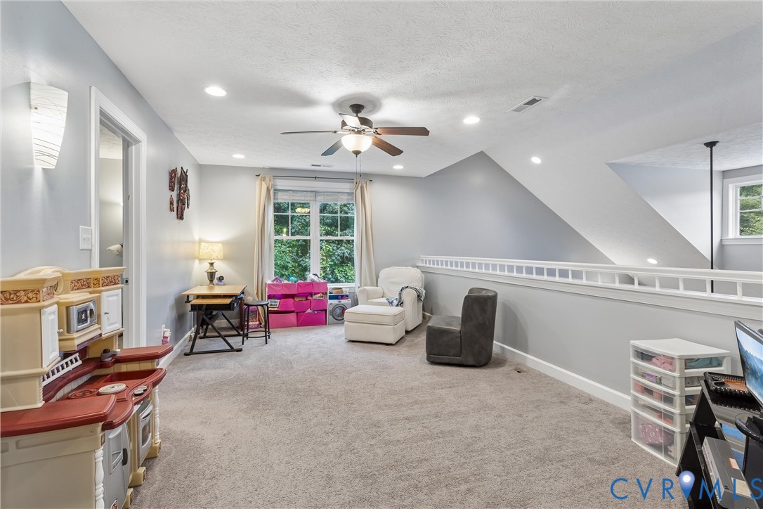 Vaulted ceiling room featuring neutral carpeting, a central ceiling fan with integrated lighting, recessed lighting, and a white balustrade railing