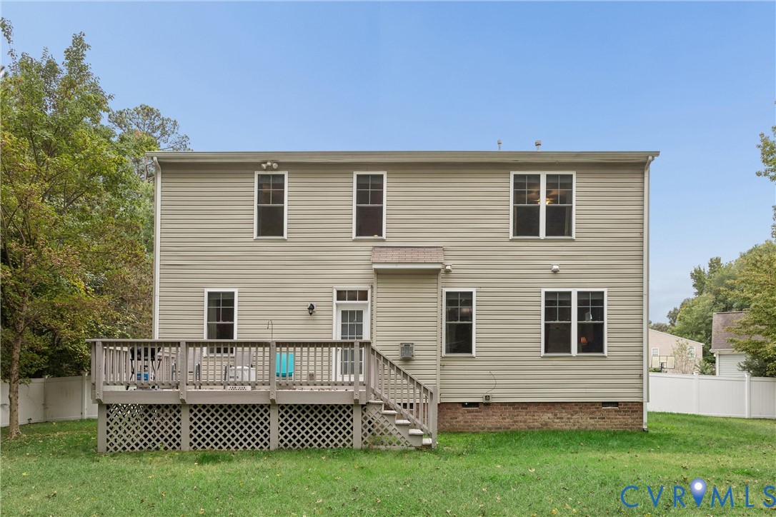 Two-story exterior featuring light-colored horizontal siding, a raised wood deck with lattice skirting, brick foundation detailing, and a white privacy fence