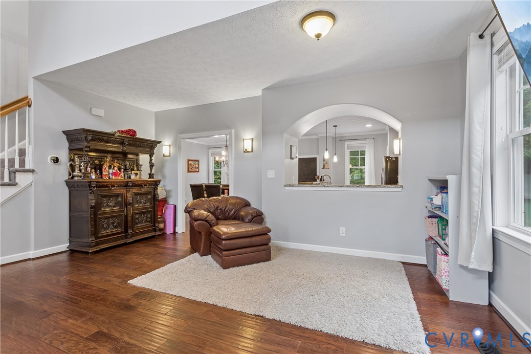 Open-concept interior featuring wood-finish flooring, a vaulted ceiling, a decorative arched pass-through, and wall-mounted sconce lighting