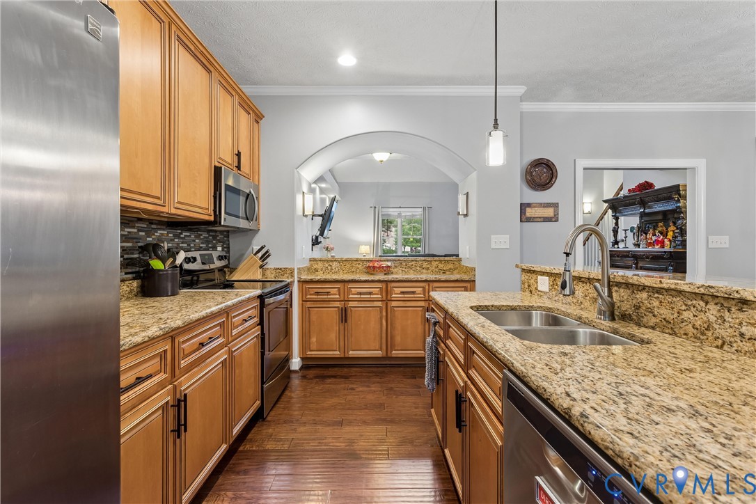 Kitchen featuring wood cabinetry, stone countertops, stainless steel appliances, a mosaic tile backsplash, and wood-finish flooring