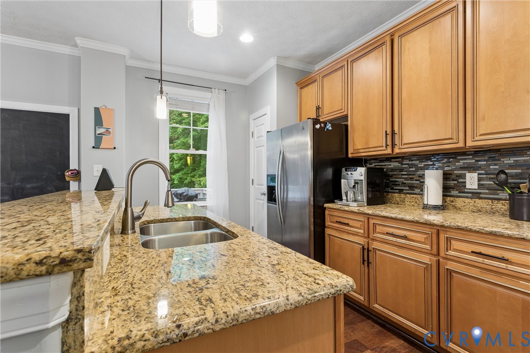 Kitchen featuring wood cabinetry, stone countertops, a dual-basin undermount sink with a gooseneck faucet, and a multi-toned tile backsplash