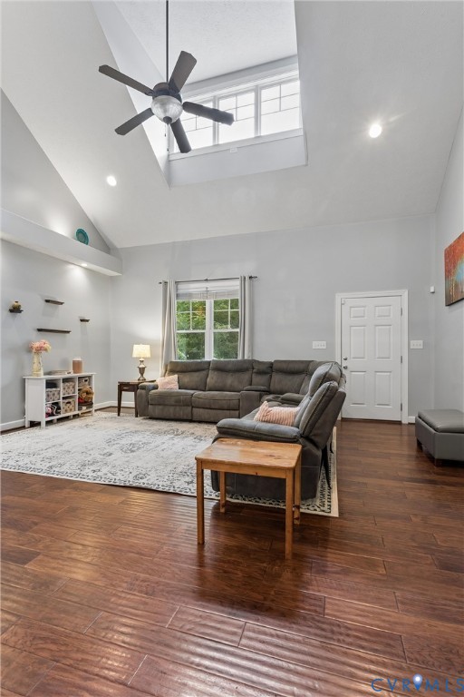Vaulted ceiling featuring a central skylight, wood-finish flooring, and a ceiling fan with integrated lighting