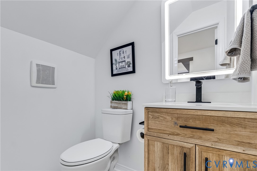 Wood-finish vanity cabinet, solid surface countertop, matte black faucet, and rectangular LED-backlit mirror