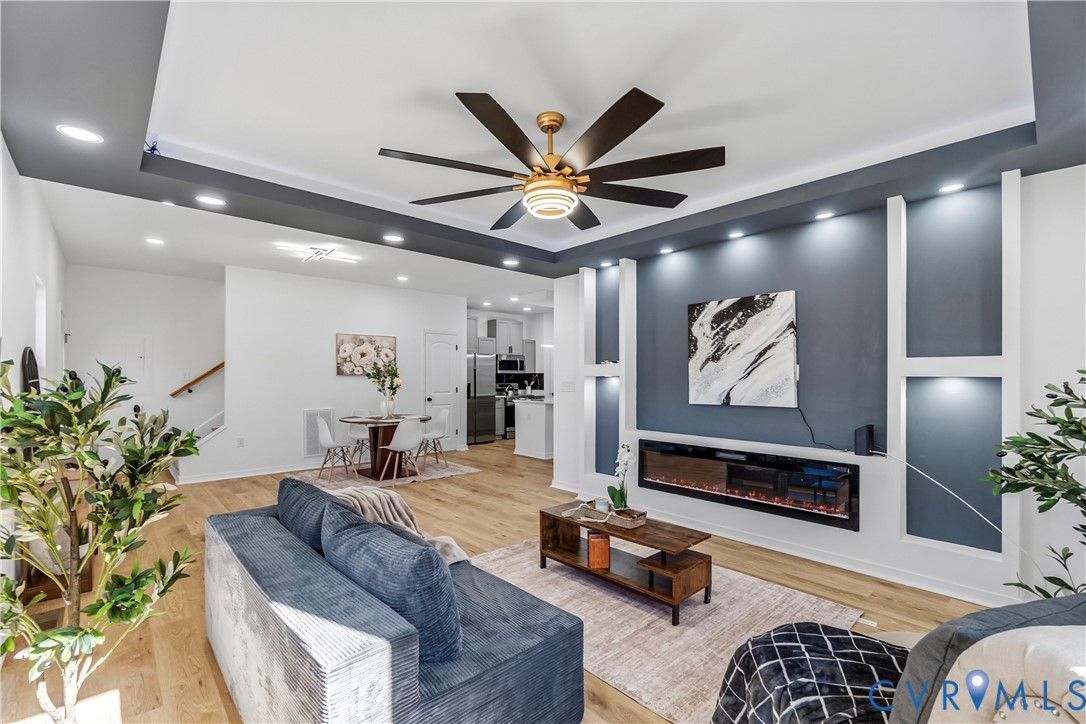 Tray ceiling with recessed lighting, integrated accent wall with built-in shelving, linear electric fireplace, and wood-finish flooring