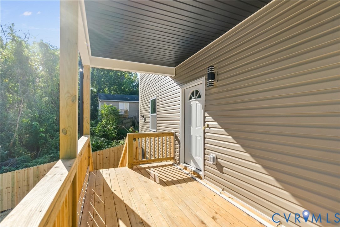 Covered exterior deck with wood-finish decking, natural wood railings, and horizontal light-toned siding