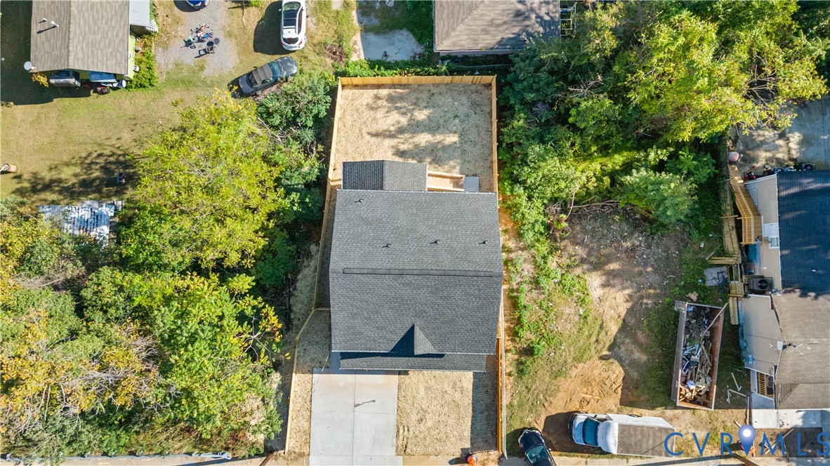Aerial perspective of the property featuring a concrete driveway, shingle-style roof, and fenced rear grounds