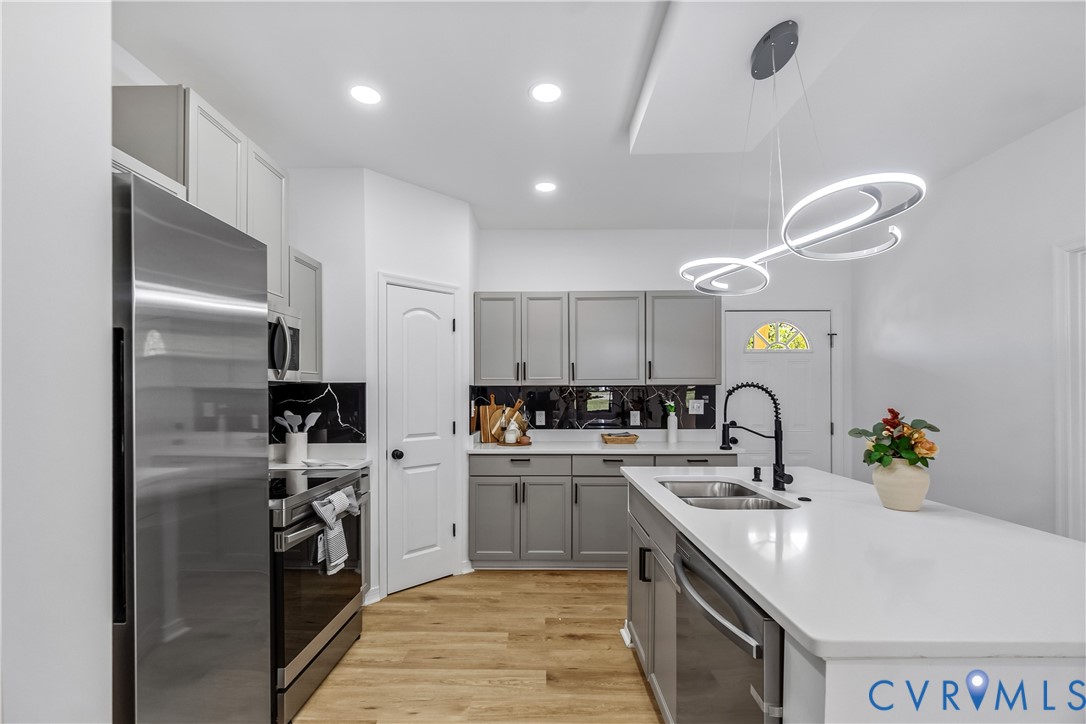 Kitchen featuring grey shaker-style cabinetry, quartz countertops, a central island with a double-basin sink, stainless steel appliances, and wood-finish flooring