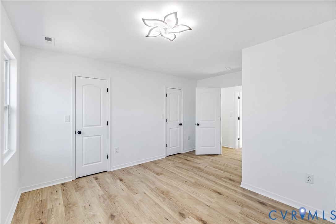 Room featuring wood-finish flooring, white walls, multiple two-panel interior doors with black hardware, and a modern floral-inspired flush-mount ceiling light fixture
