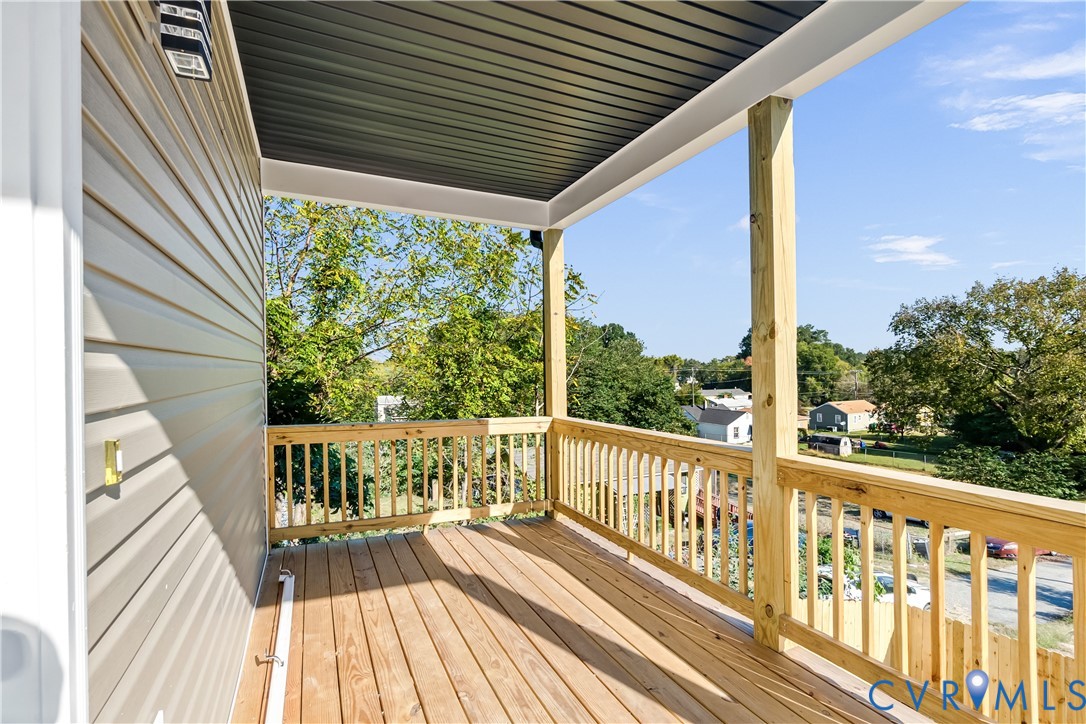 Covered balcony featuring wood-finish decking, light-tone wood railing, and vinyl siding