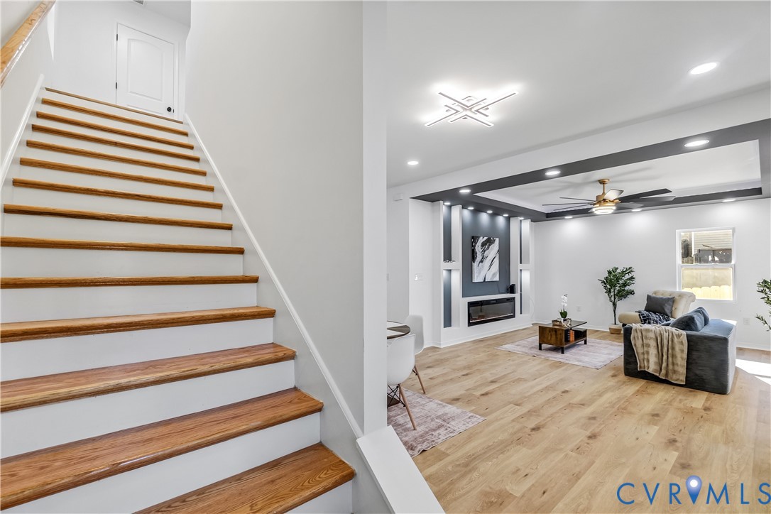 Staircase featuring wood-finish treads and white risers, wood-finish flooring, recessed lighting, built-in electric fireplace with decorative shelving, and a ceiling fan with integrated lighting