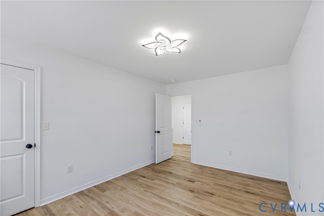 Room with wood-finish flooring, white walls, two-panel interior doors with matte black hardware, and a floral-inspired flush mount ceiling light fixture