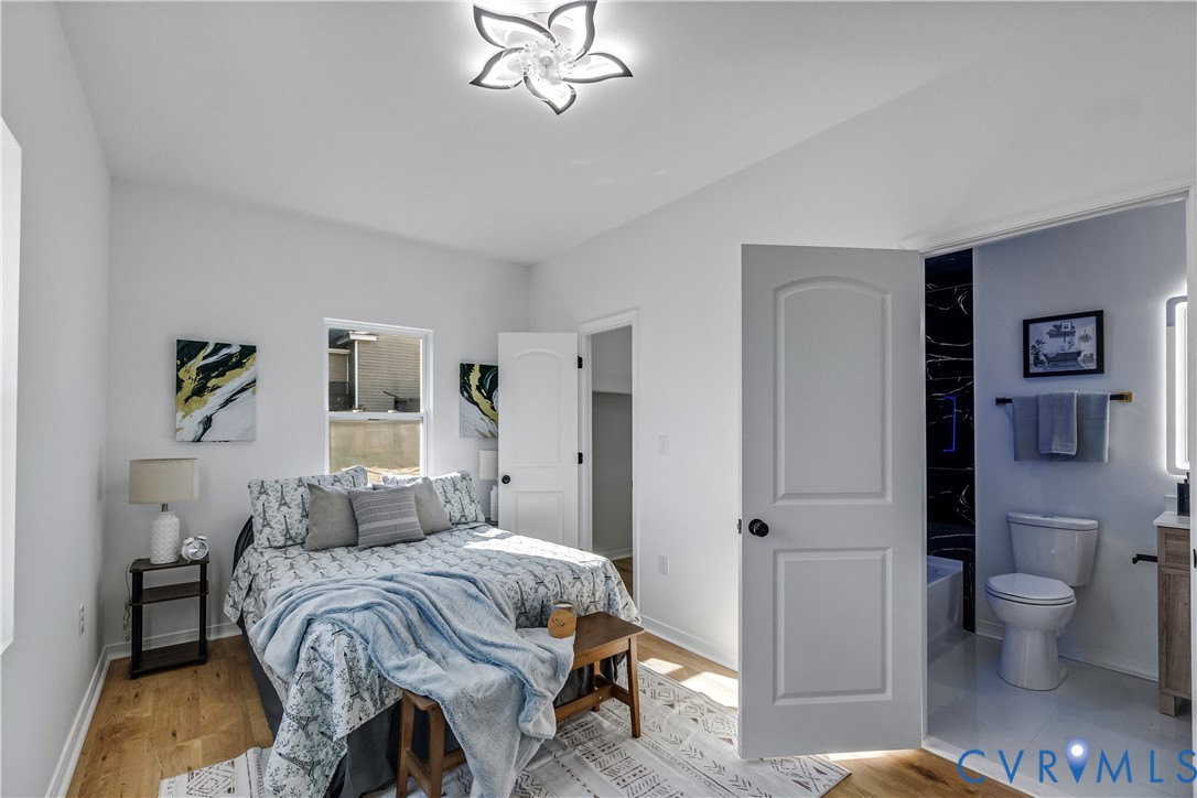 Wood-finish flooring, decorative floral-style ceiling light fixture, and arched-panel interior doors, with an entryway into a bathroom featuring high-contrast tiling