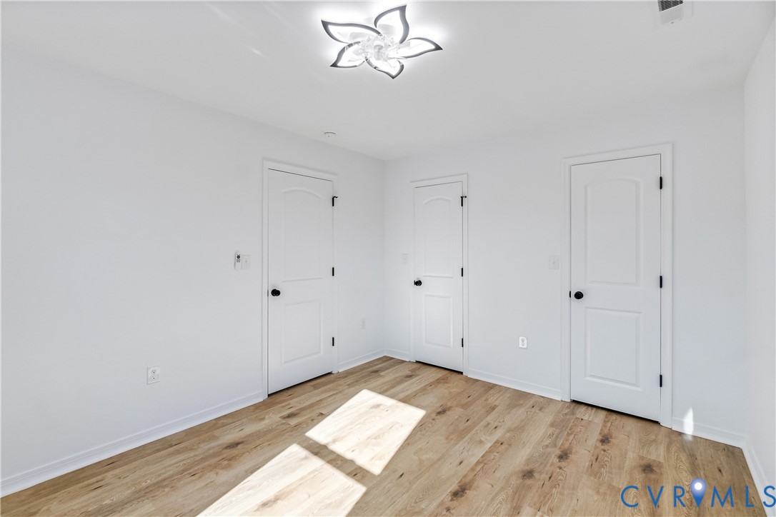 Wood-finish flooring, three-panel interior doors with matte black hardware, and a contemporary petal-style flush-mount ceiling fixture