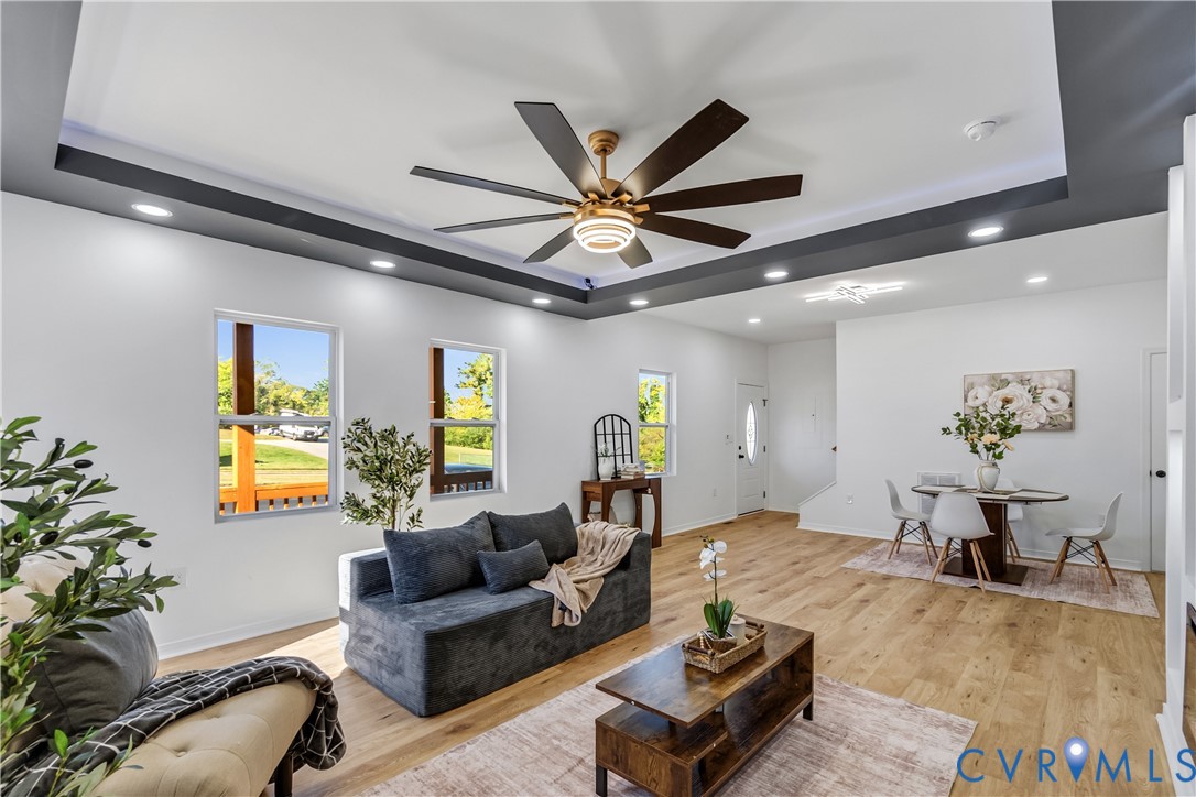 Tray ceiling with dark-toned trim, expansive multi-blade ceiling fan, wood-finish flooring, and recessed lighting