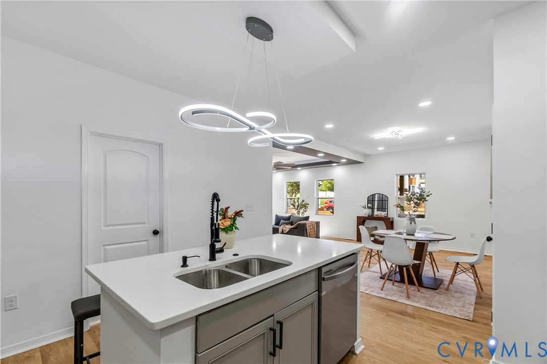 Kitchen island featuring a quartz countertop, dual-basin stainless steel sink, matte black gooseneck faucet, grey cabinetry, and geometric LED pendant lighting