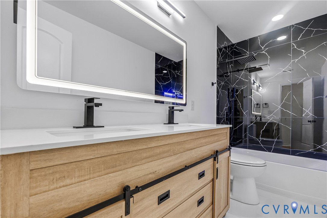 Wood-finish dual vanity with sliding barn-style doors, rectangular vessel sinks, matte black hardware, integrated LED-backlit mirror, and full-height wall tile with marble-patterned finish