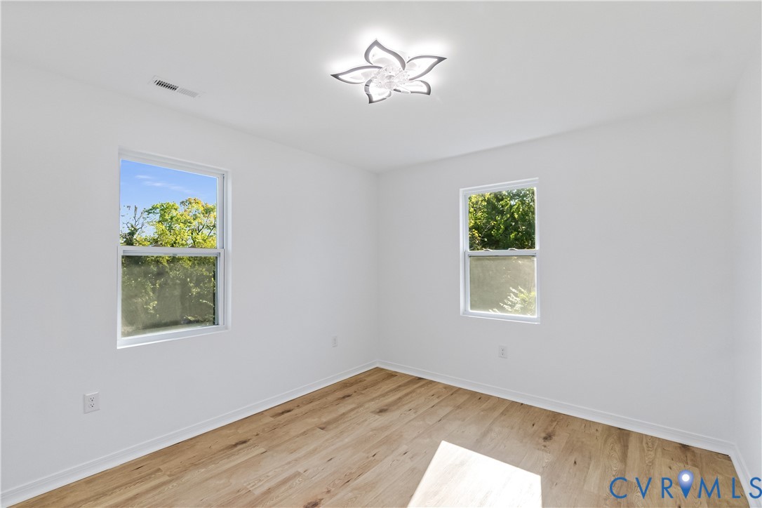 Bright room featuring light wood-finish flooring, two large windows, and a decorative floral-inspired ceiling fixture
