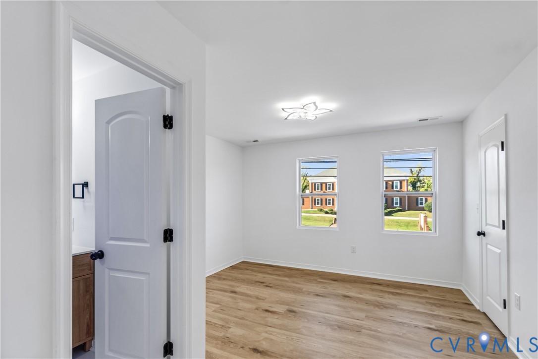 Interior room featuring wood-finish flooring, two double-hung windows, white arched-panel doors, and a contemporary floral-style flush-mount ceiling light