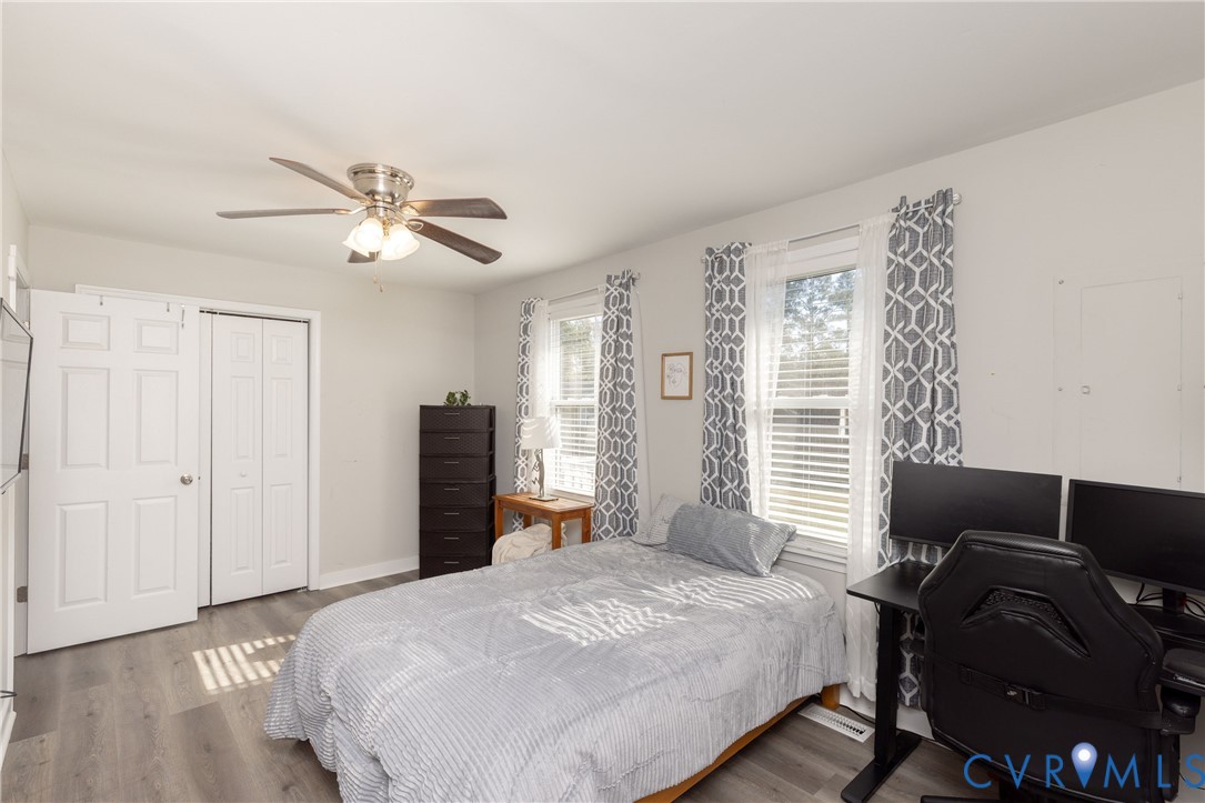 Room featuring wood-finish flooring, dual windows, ceiling fan with integrated lighting, and dual-panel closet doors