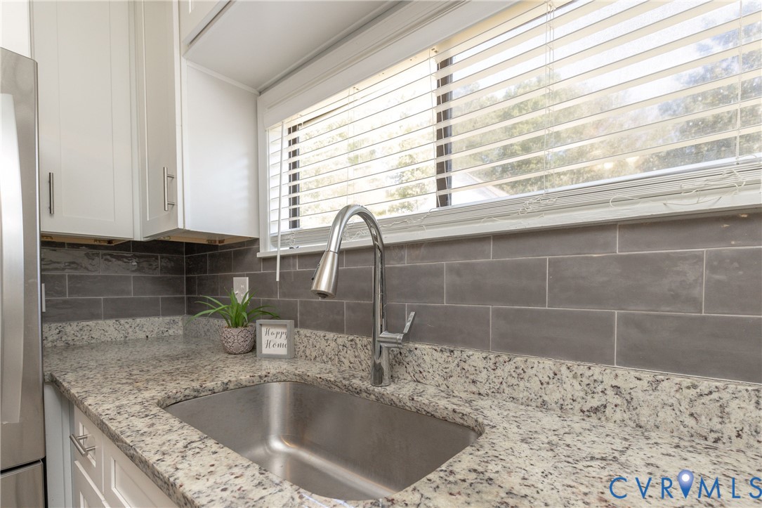 Kitchen featuring stone countertops, stainless steel undermount sink, gooseneck faucet, gray subway tile backsplash, and white cabinetry