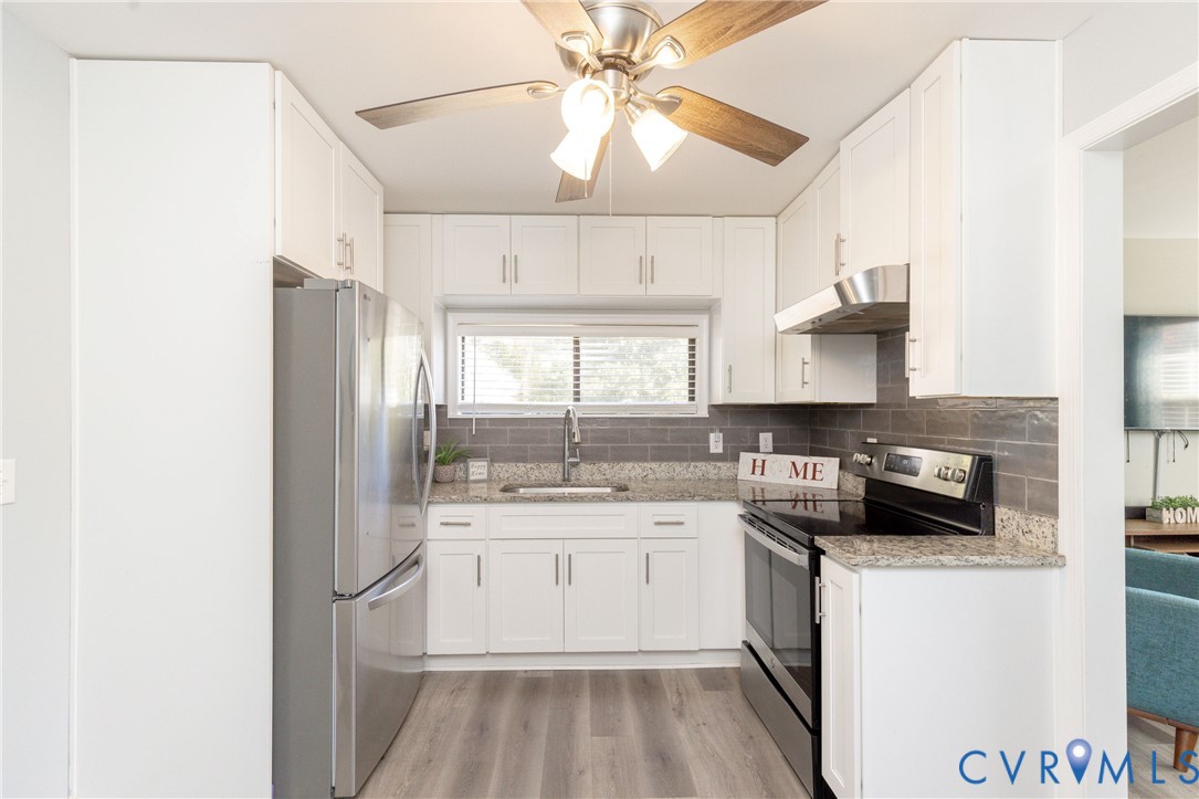 Kitchen featuring white cabinetry, stone-surface countertops, subway tile backsplash, stainless steel appliances, and wood-finish flooring
